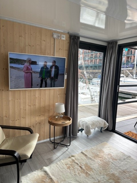 Wood-panelled living room with wall-mounted TV, armchair, sheepskin rug and glass doors to the marina